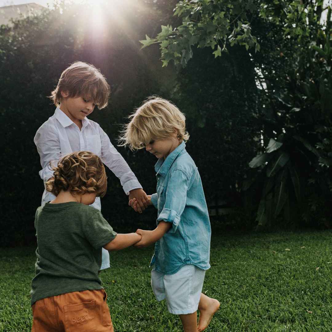 Three boys holding hands in a circle outside on the grass
